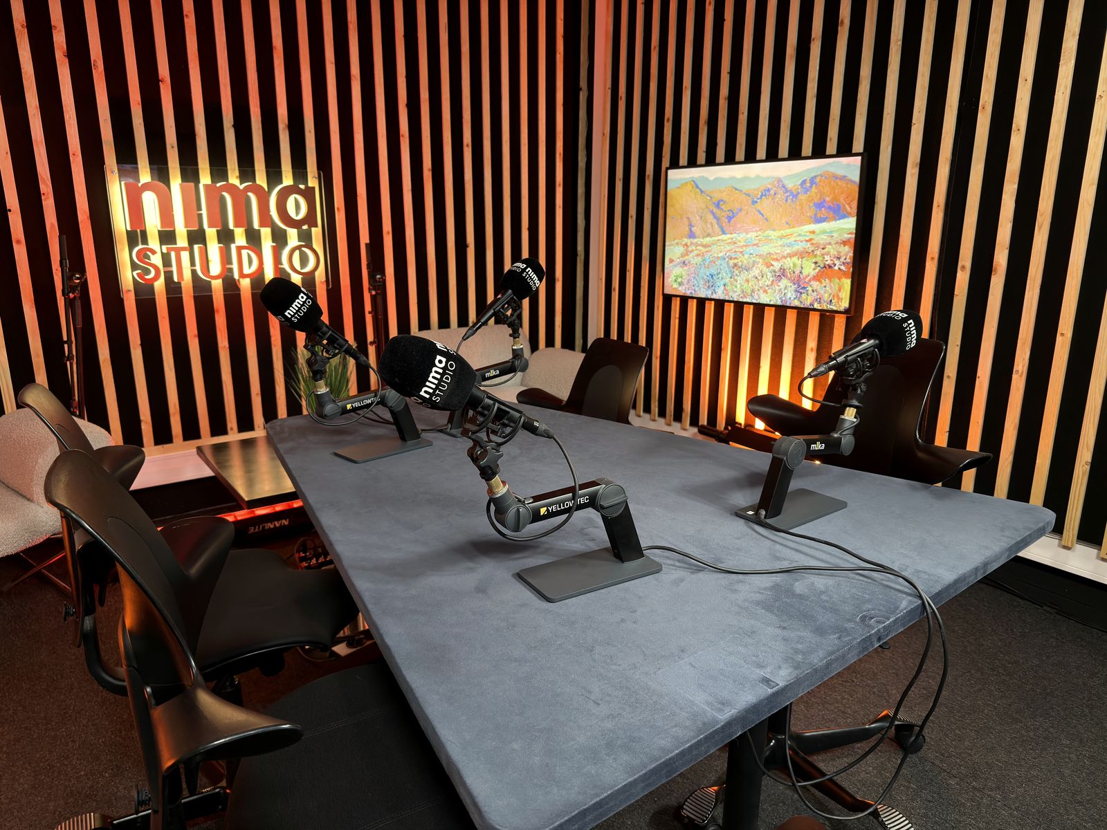 Podkaststudio B med lyssatt Nima Studio-skilt og fire mikrofoner